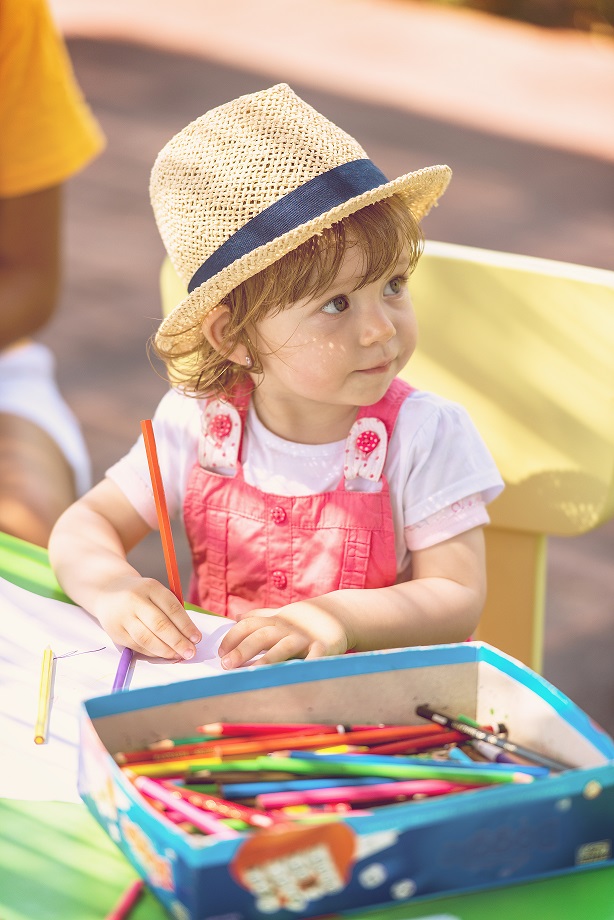 little girl using pencil crayons while drawing a colorful pictures in the outside playschool