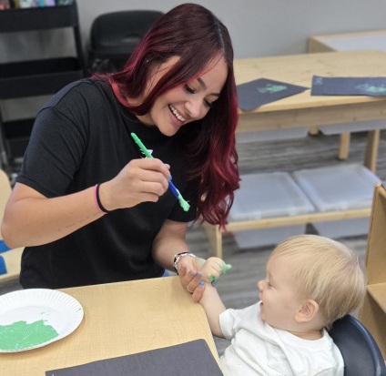 Ms Debany painting toddler's hand
